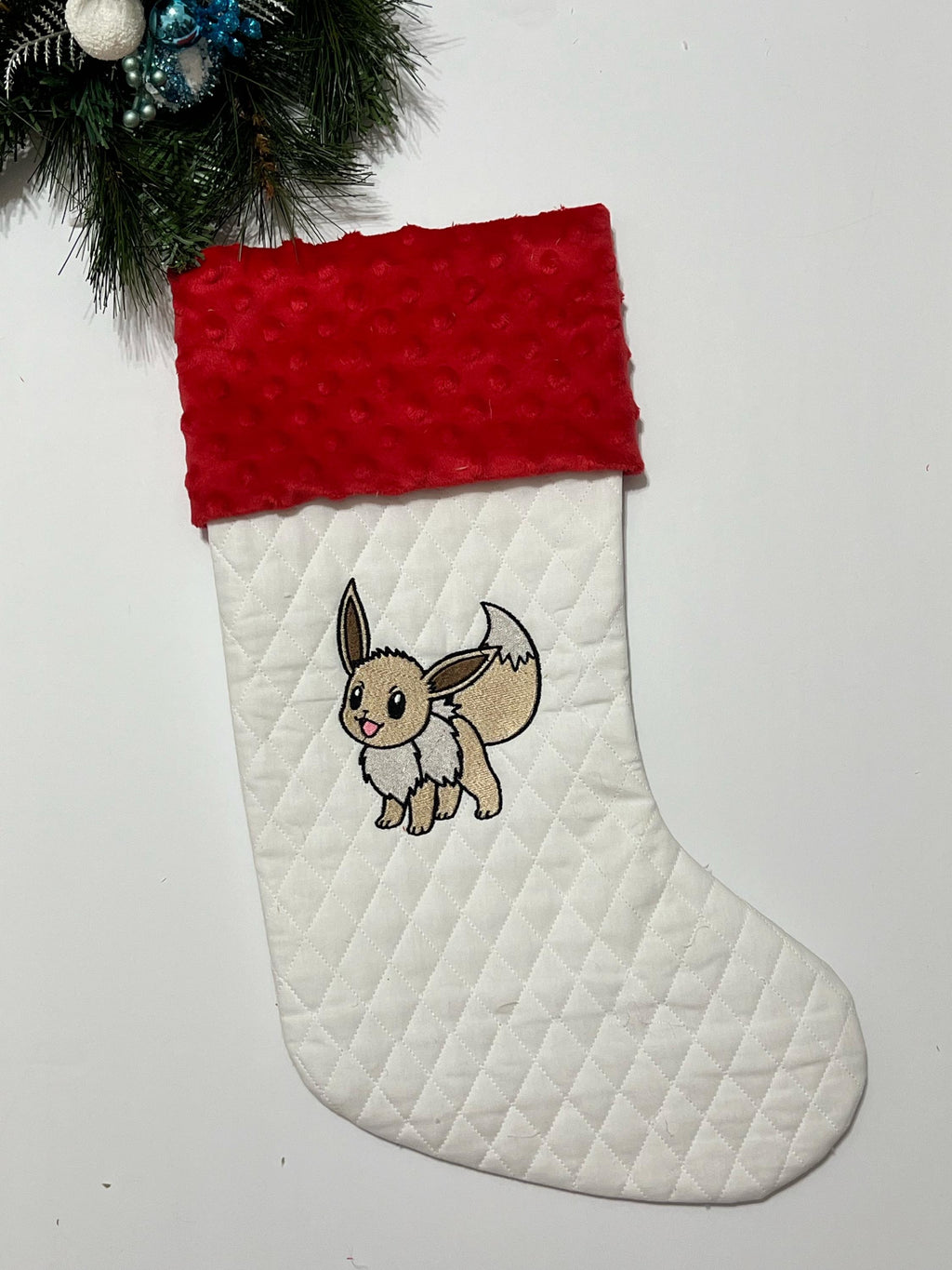 Personalized Christmas stocking made from white quilted fabric featuring embroidered Eevee evolution on front, fully lined, and minky cuff