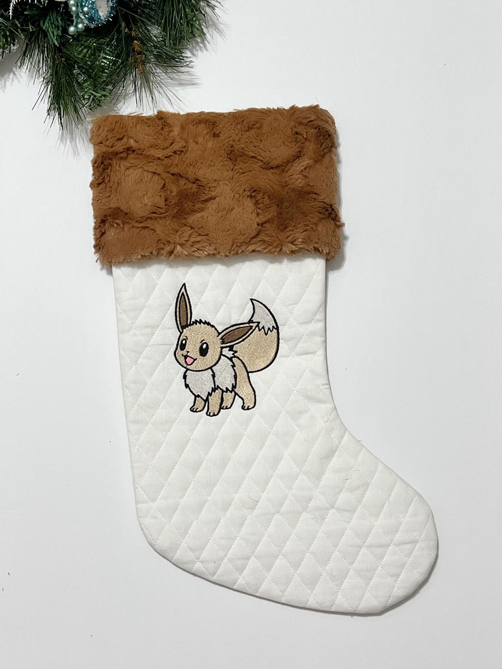 Personalized Christmas stocking made from white quilted fabric featuring embroidered Eevee evolution on front, fully lined, and minky cuff