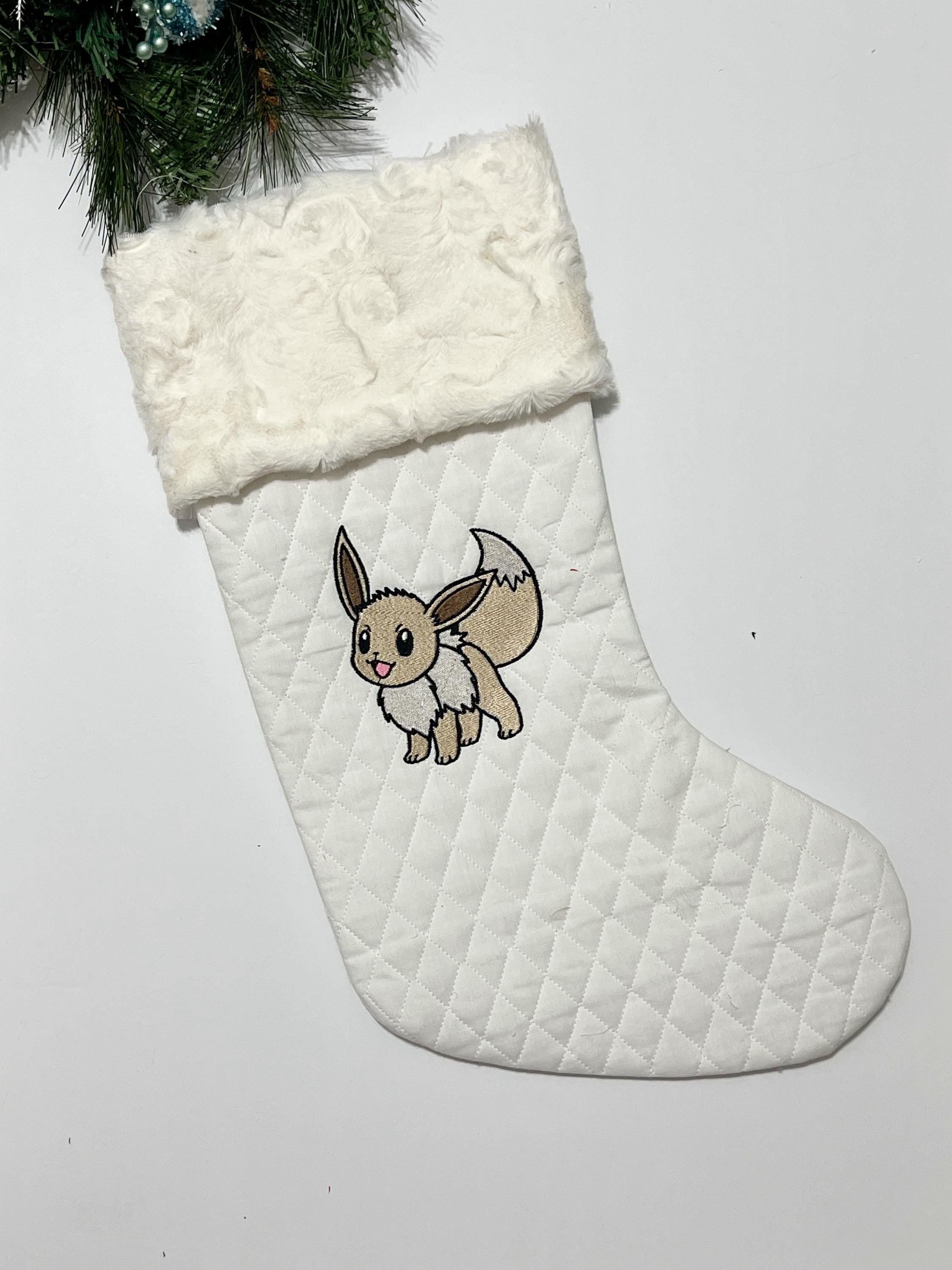 Personalized Christmas stocking made from white quilted fabric featuring embroidered Eevee evolution on front, fully lined, and minky cuff